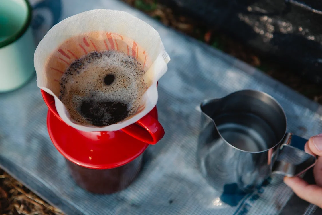 Close up of paper coffee filter with a metal pitcher on the side.