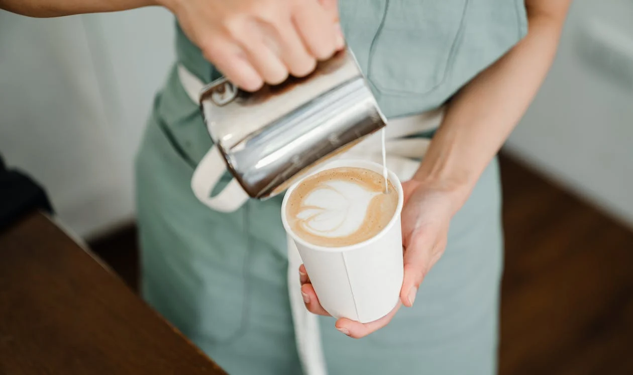 Person creating tulip latte art by pouring milk on cup of coffee