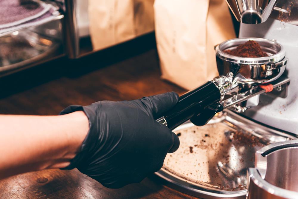 A hand of barista holding portafilter coffee in cafe
