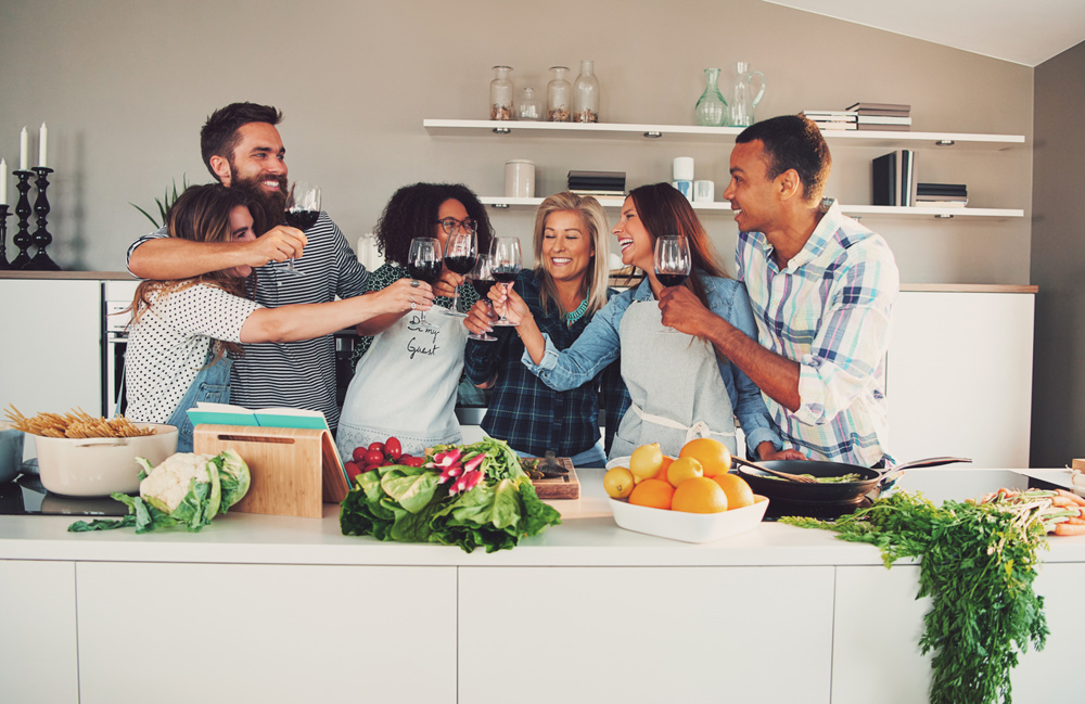 Group of young cheerful friends cheering while cooking some tasteful food in the kitchen