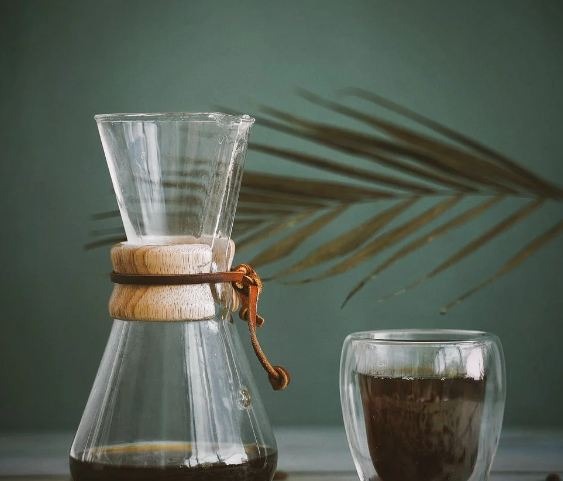 A cup of coffee with a jug of coffee and coffee beans spilled on the floor  