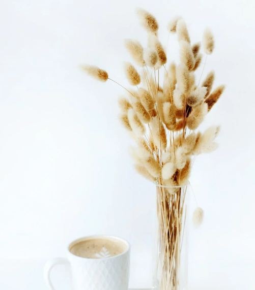 A cup of white coffee on a tray with a vase full of flowers