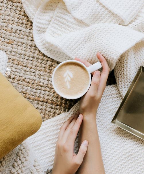 A person having a white coffee on their bed with blanket