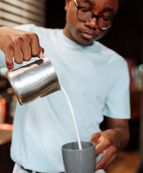 A person pouring milk in coffee
