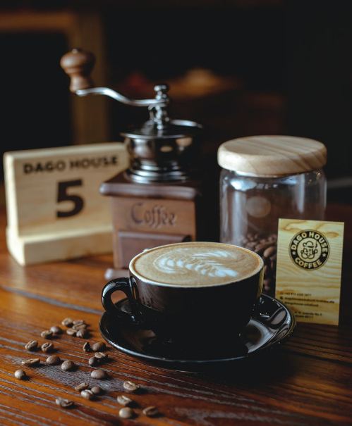 A cup of coffee on a table with a jar full of coffee beans  