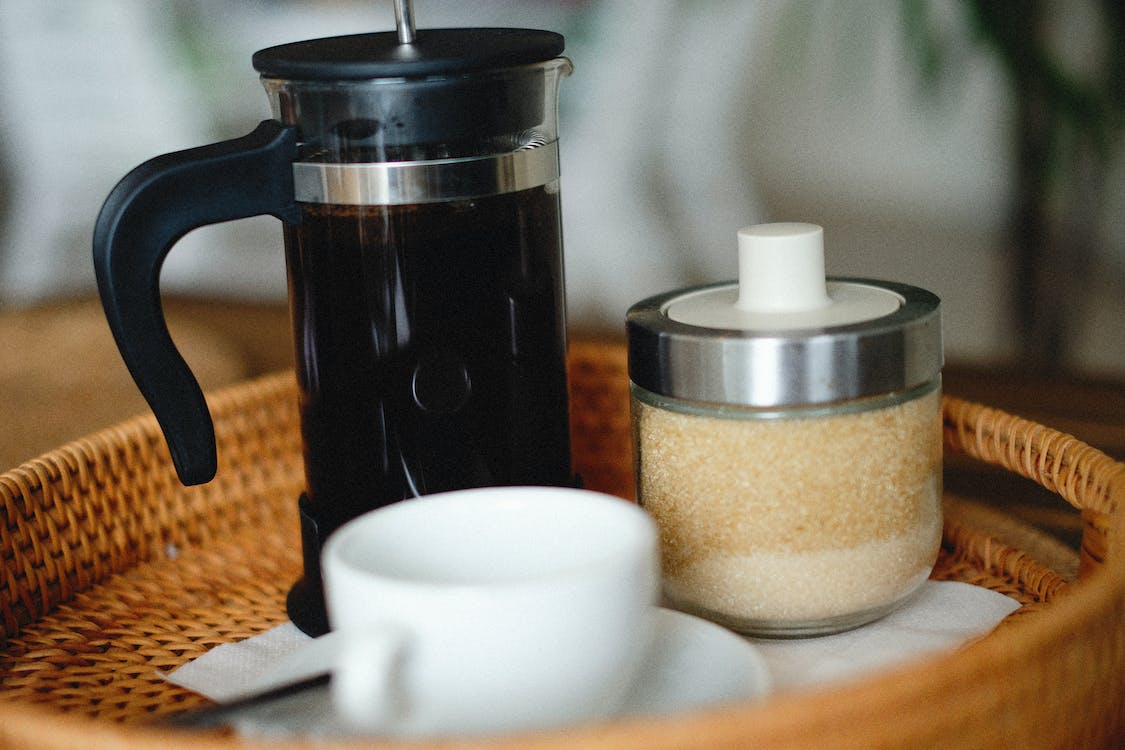 Close up of French-press style coffee maker on tray with cup and jar of sugar