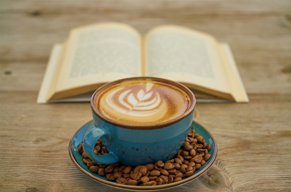 a blue coffee mug with coffee and coffee beans and a book in the background