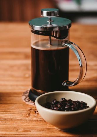 a French press beside a bowl of coffee beans