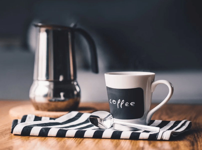 a coffee mug, teaspoon, and a thermos on a table