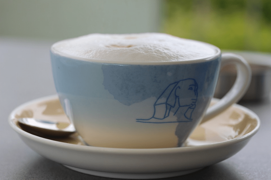 a white, sky-blue cup and saucer, with froth on its mouth