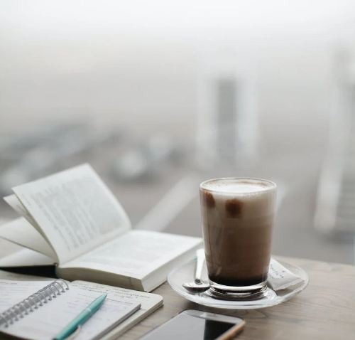 A cup of cold coffee on a table with a book and phone
