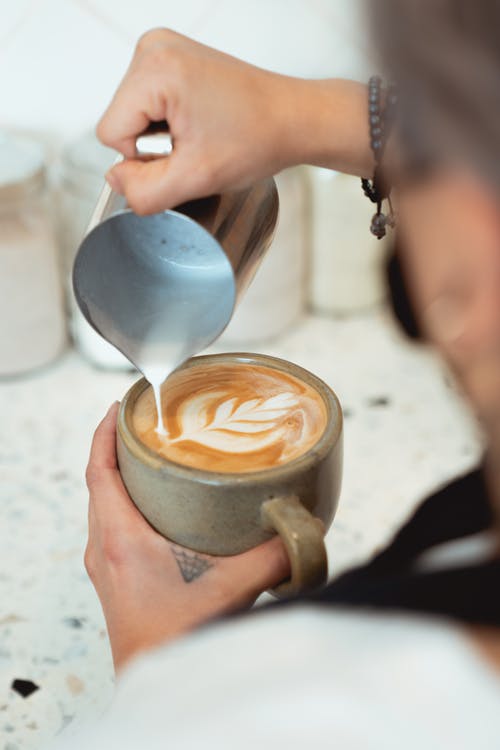 a person pouring milk from a pitcher on a cup of coffee. 
