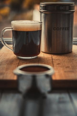 Image showing a glass of black coffee and coffee canister on a wooden table.