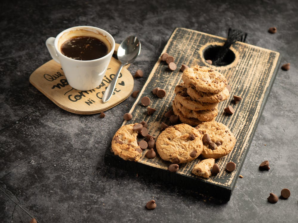 A cup of coffee and a plate full of chocolate chip cookies on table