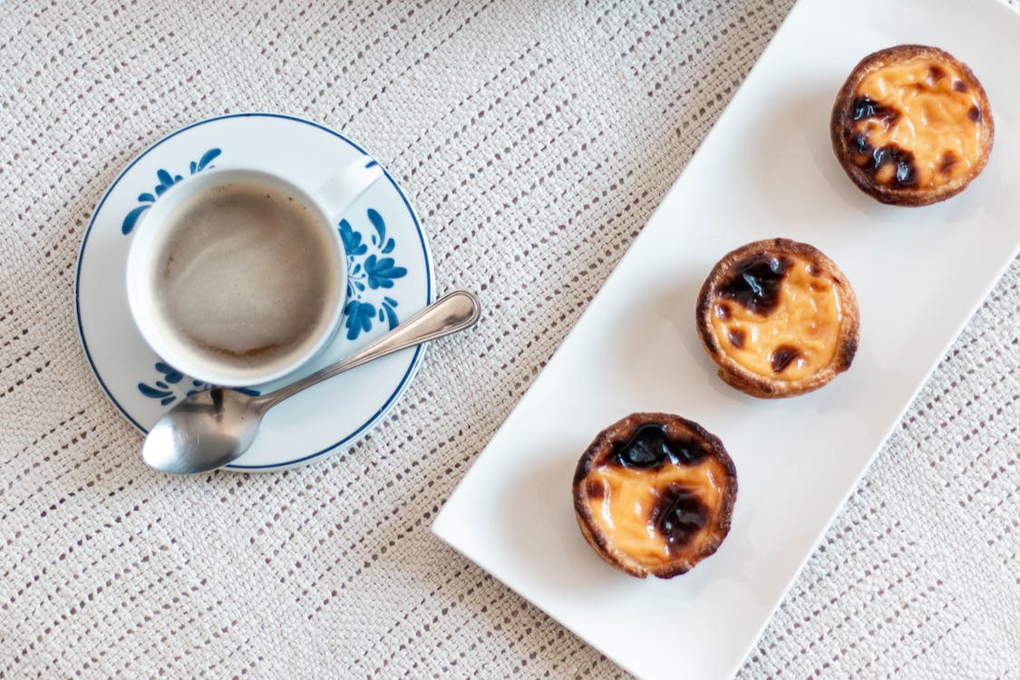 A cup of coffee and a tray of tarts on a table