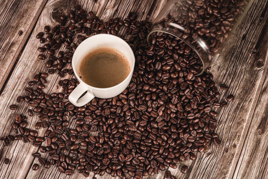 A cup of coffee on surface with coffee beans scattered around