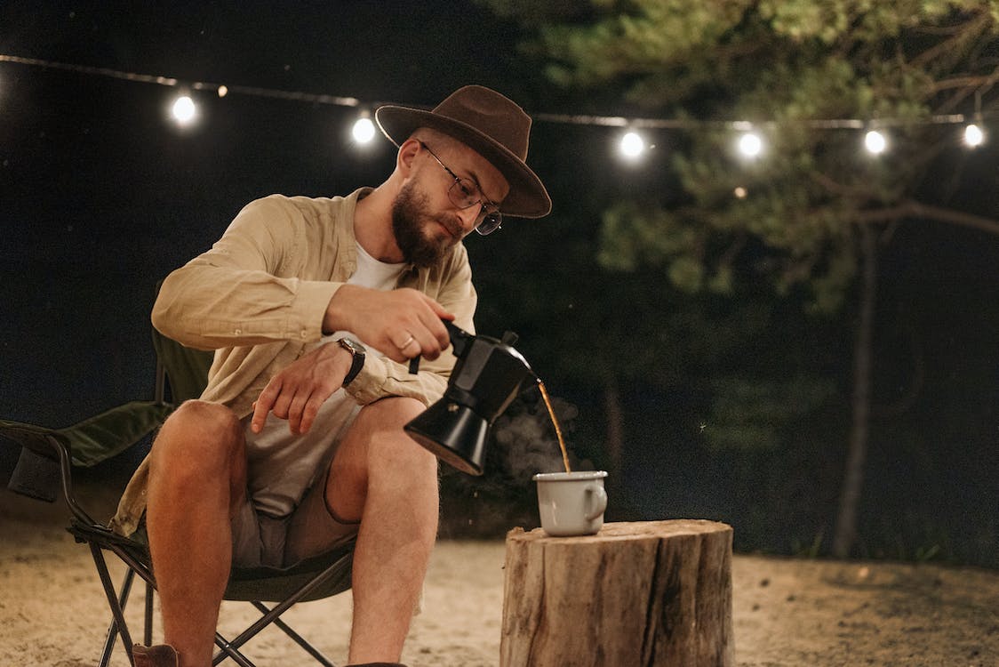 A man pouring coffee from a portable coffee maker outside at night
