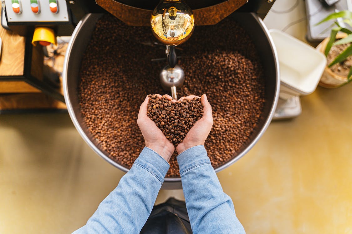 A person holding coffee beans with coffee equipment in the background