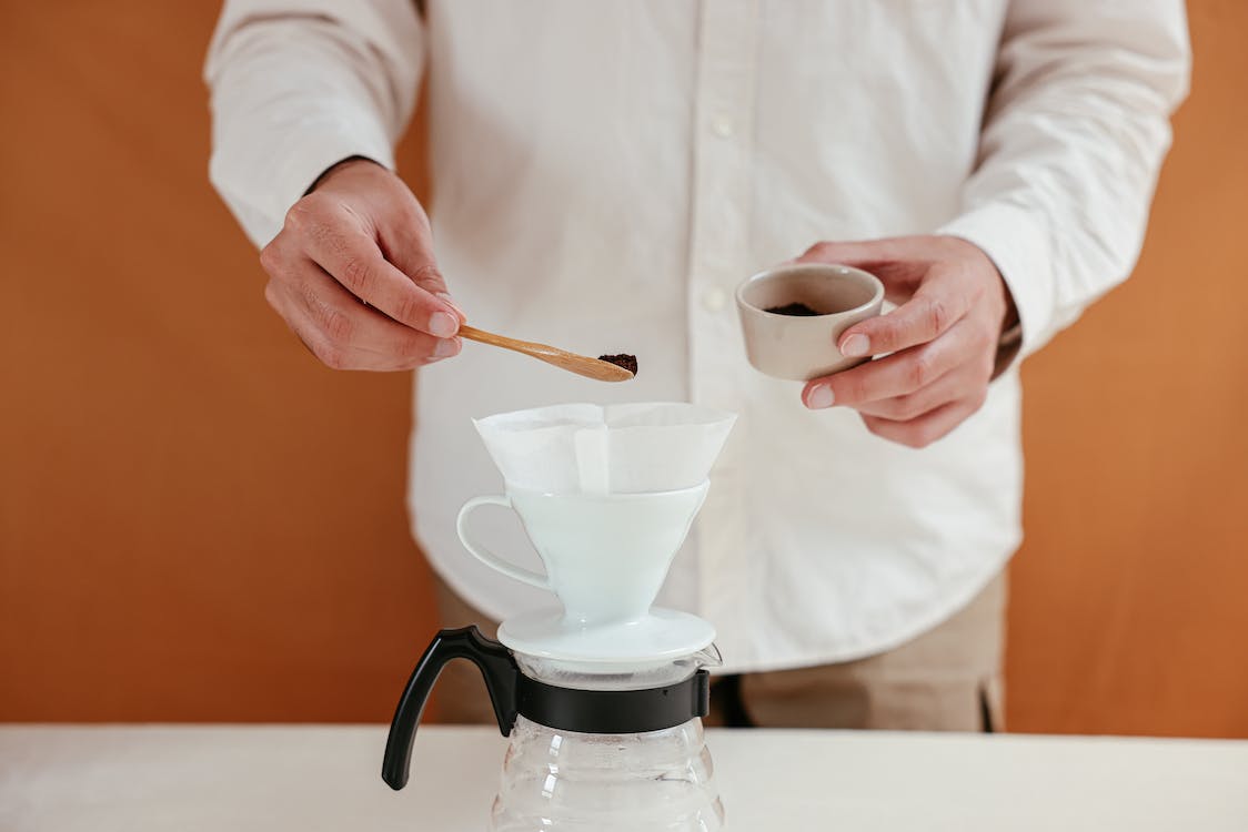 Person pouring coffee grains on coffee dripper