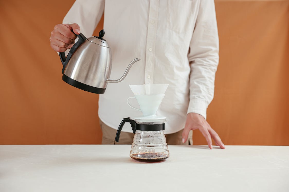 Person pouring hot water on coffee dripper with a gooseneck kettle